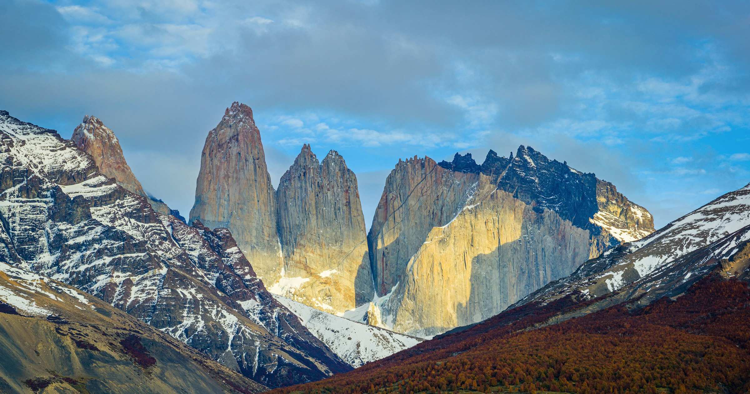 Dramatic granite towers of Torres del Paine in the Chilean Andes, with autumn foliage and Patagonian peaks at golden hour