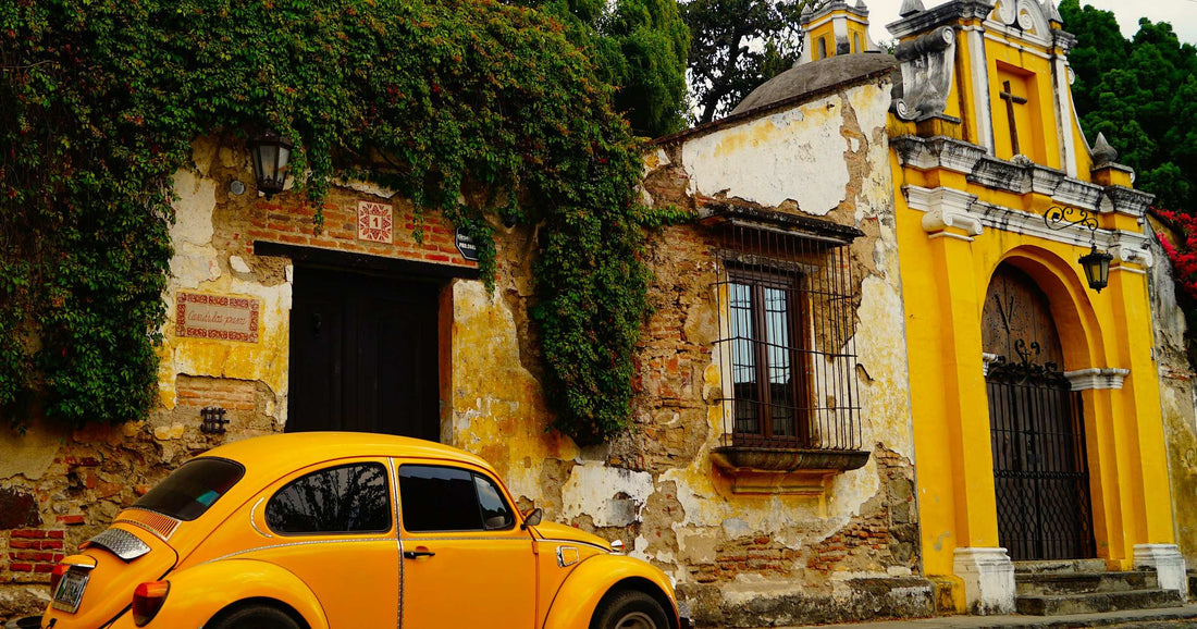 Classic yellow Volkswagen Beetle on a cobblestone street in Antigua, Guatemala, framed by colonial yellow-facade architecture