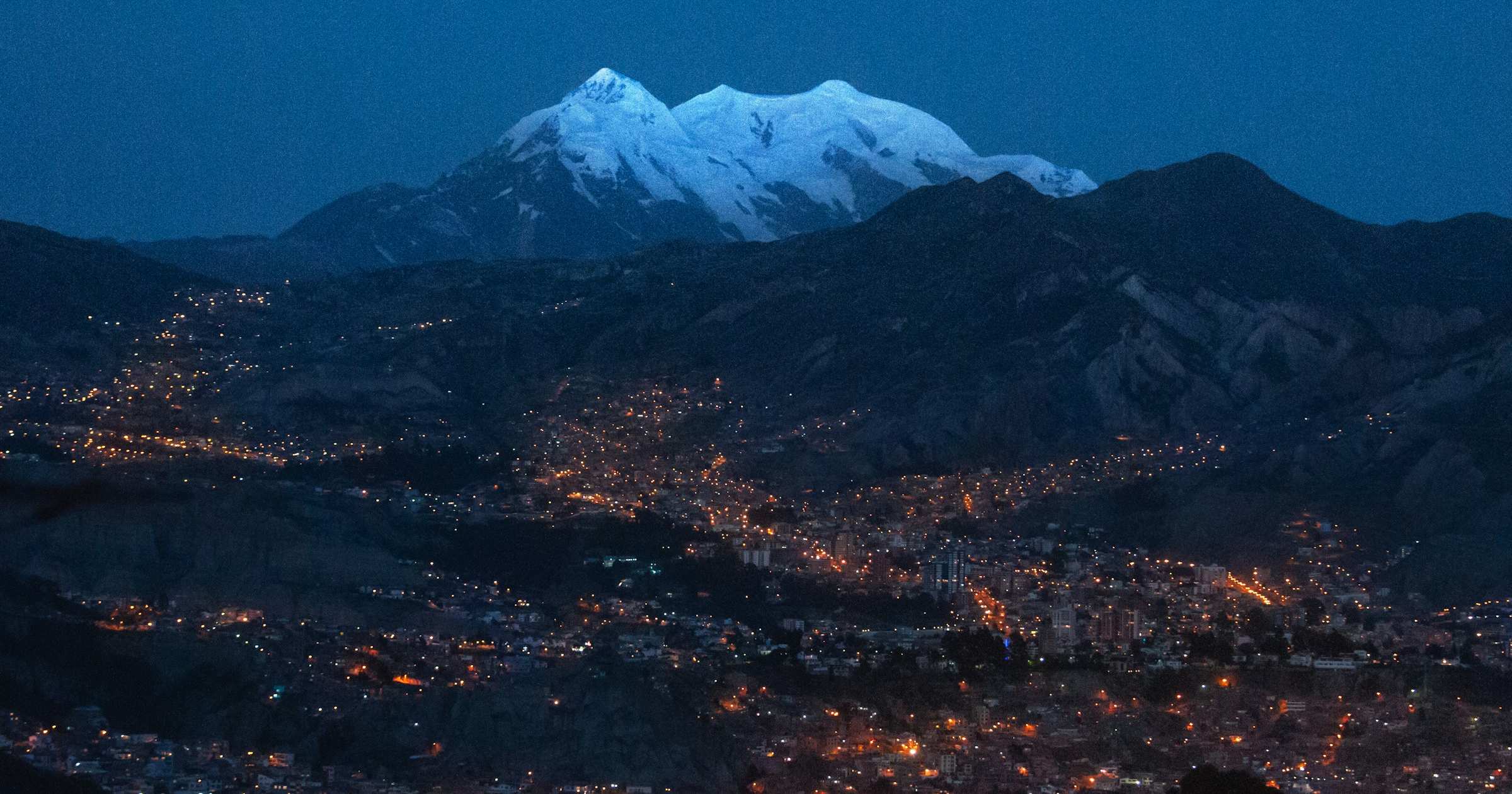 La Paz at twilight beneath snow-capped Illimani peak in the Bolivian Andes — the high-altitude landscape where travellers compare single-country versus regional eSIM coverage across Peru and Bolivia.