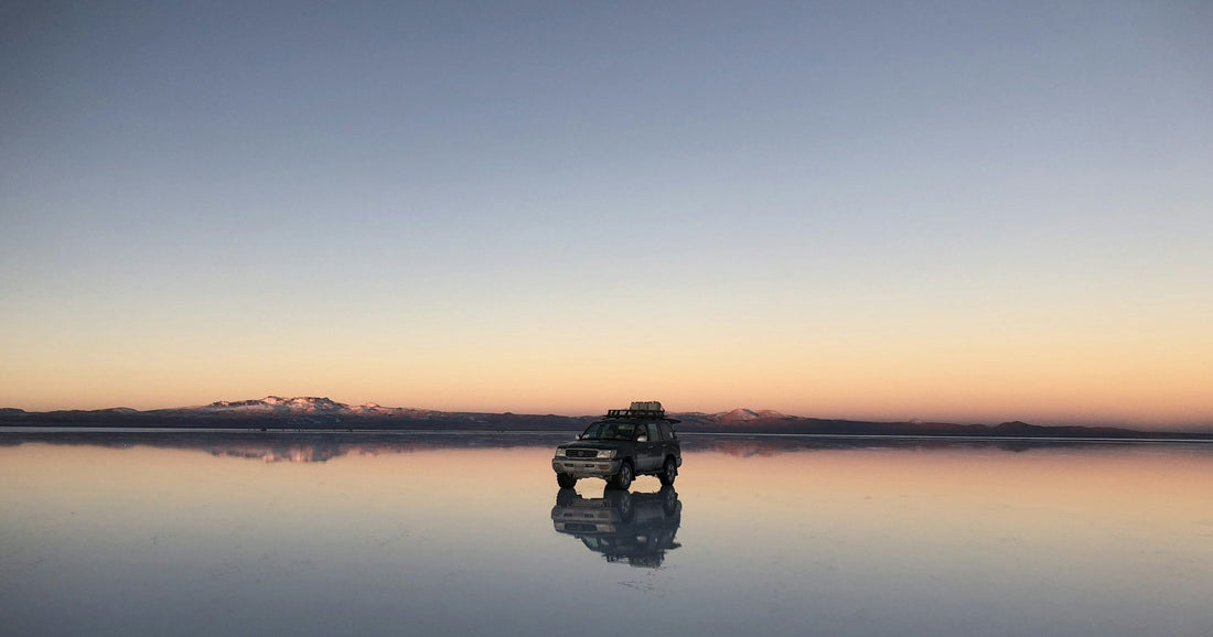 Salar de Uyuni salt flat at dusk with a 4x4 jeep and its perfect mirror reflection, Bolivia