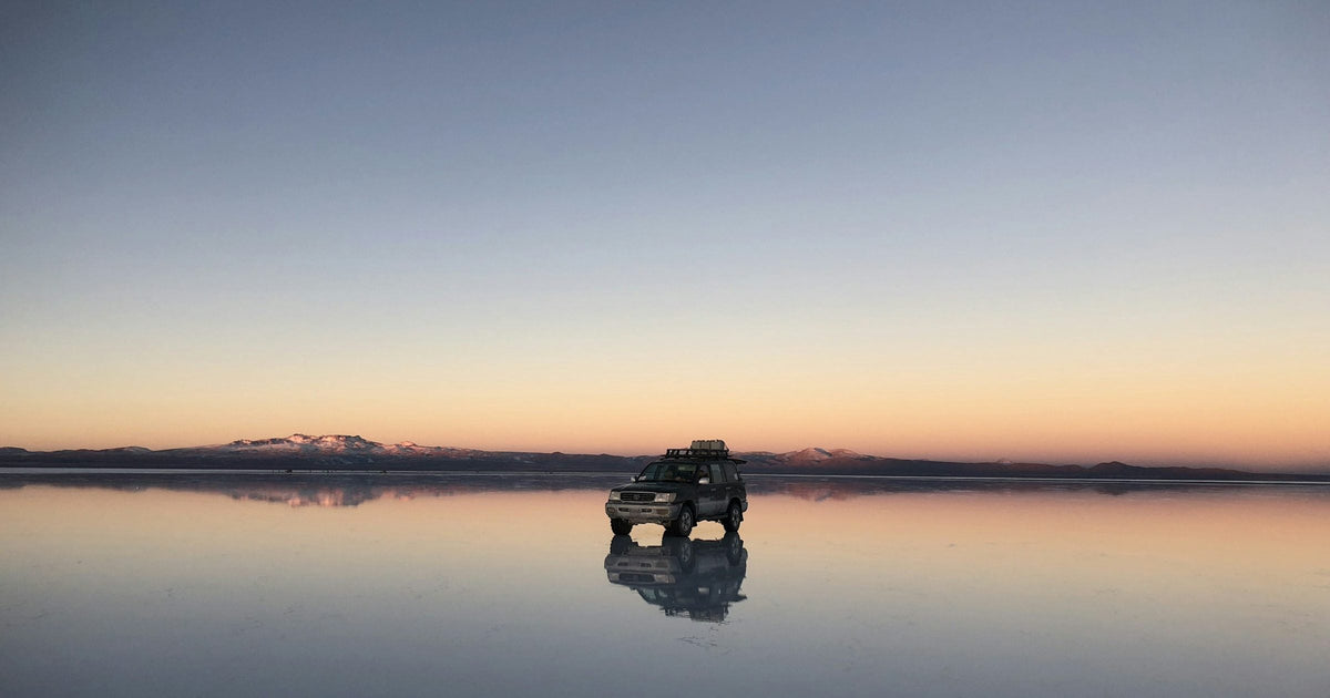 Salar de Uyuni salt flat at dusk with a 4x4 jeep and its perfect mirror reflection, Bolivia