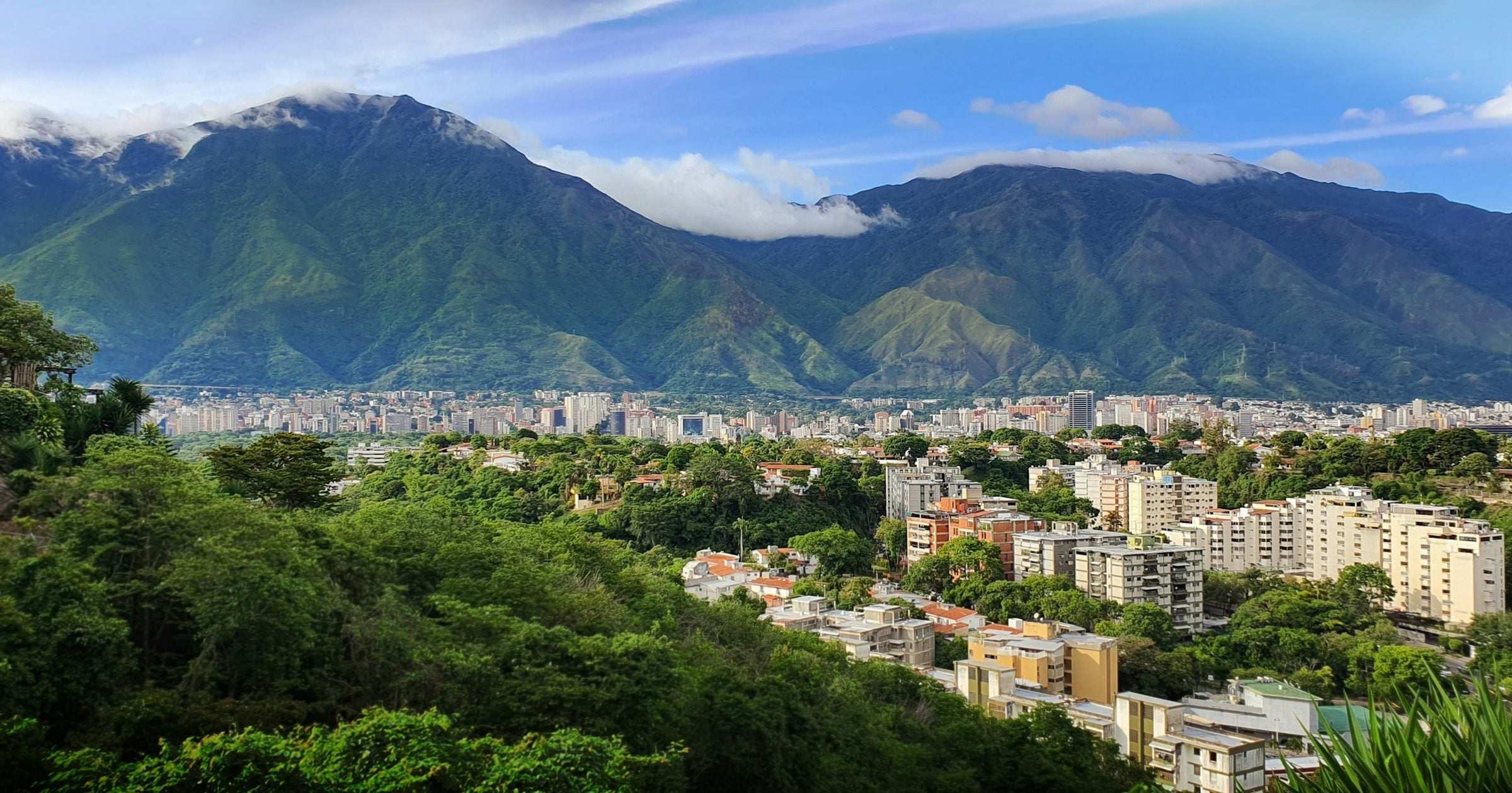 Caracas cityscape with the lush green El Avila mountain rising behind under a bright blue sky.