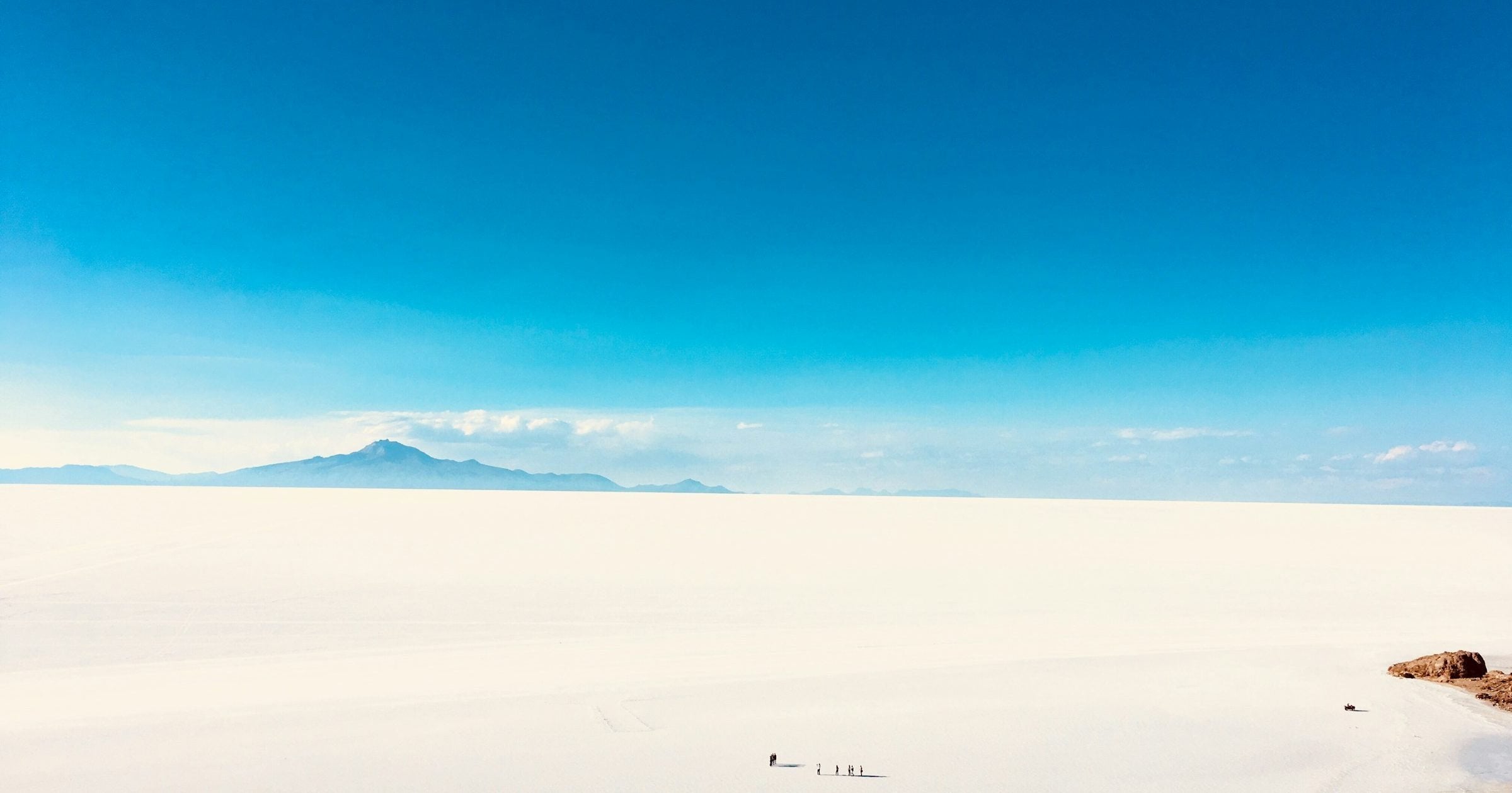 Vast white expanse of Salar de Uyuni with a distant volcano on the horizon, Bolivia