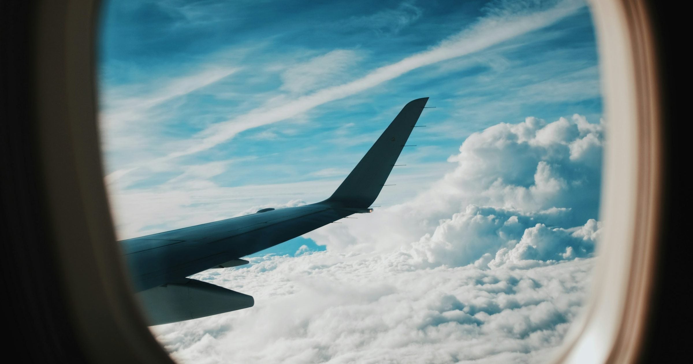Airplane window view with wing above clouds — travelling to Canada