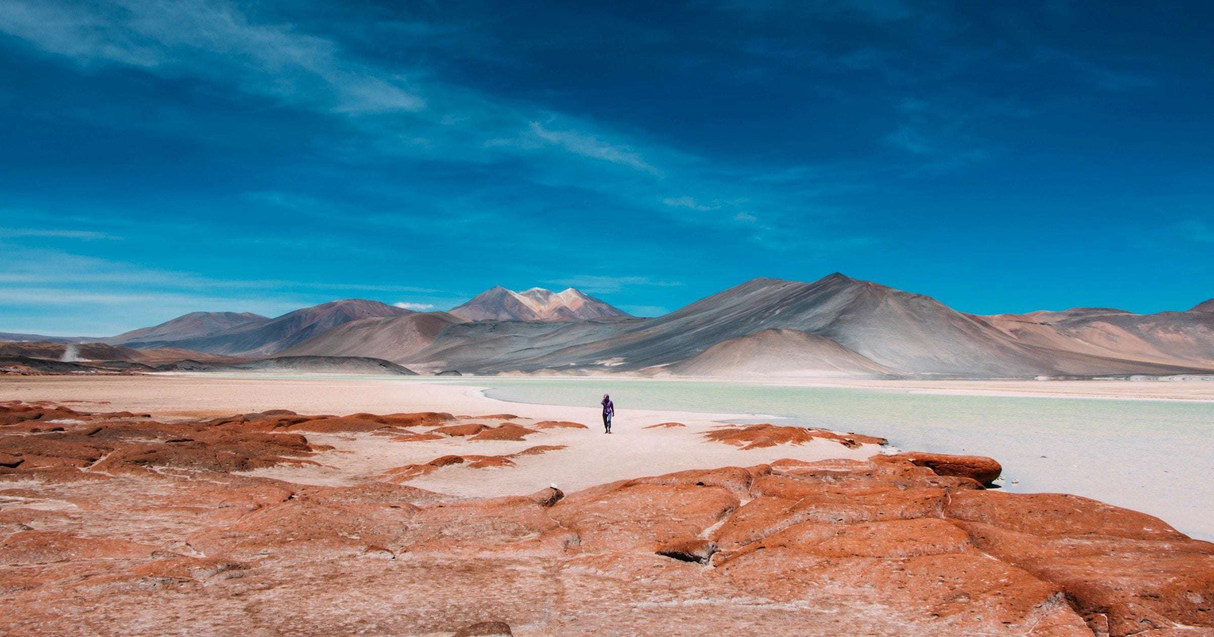 A traveller crosses red Atacama desert flats beneath snow-capped Andes — popular destination for travellers staying connected with a Chile eSIM.