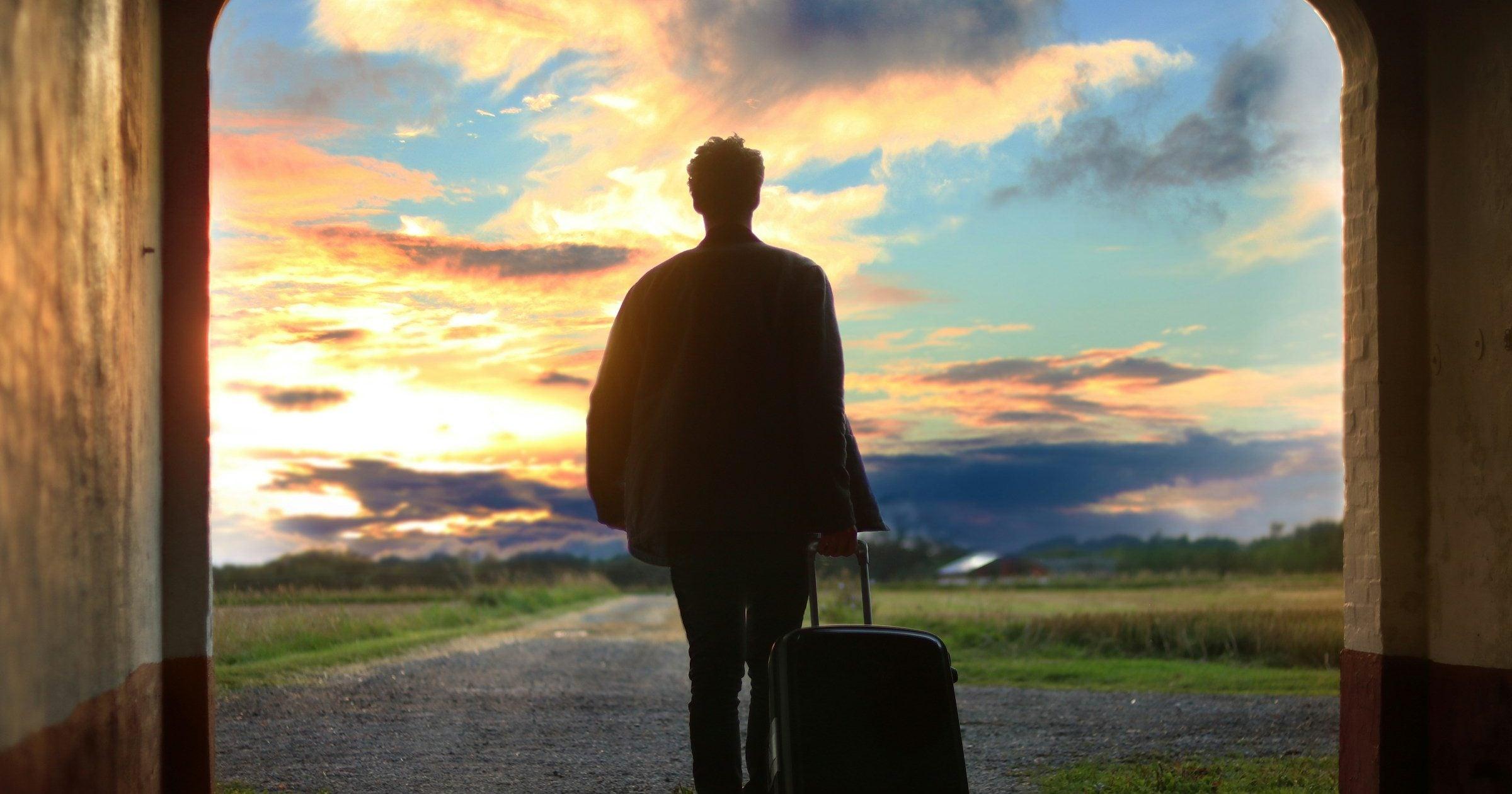 Silhouetted first-time traveller with luggage walking through an arch toward a sunset sky — the start of a journey where eSIM setup matters.