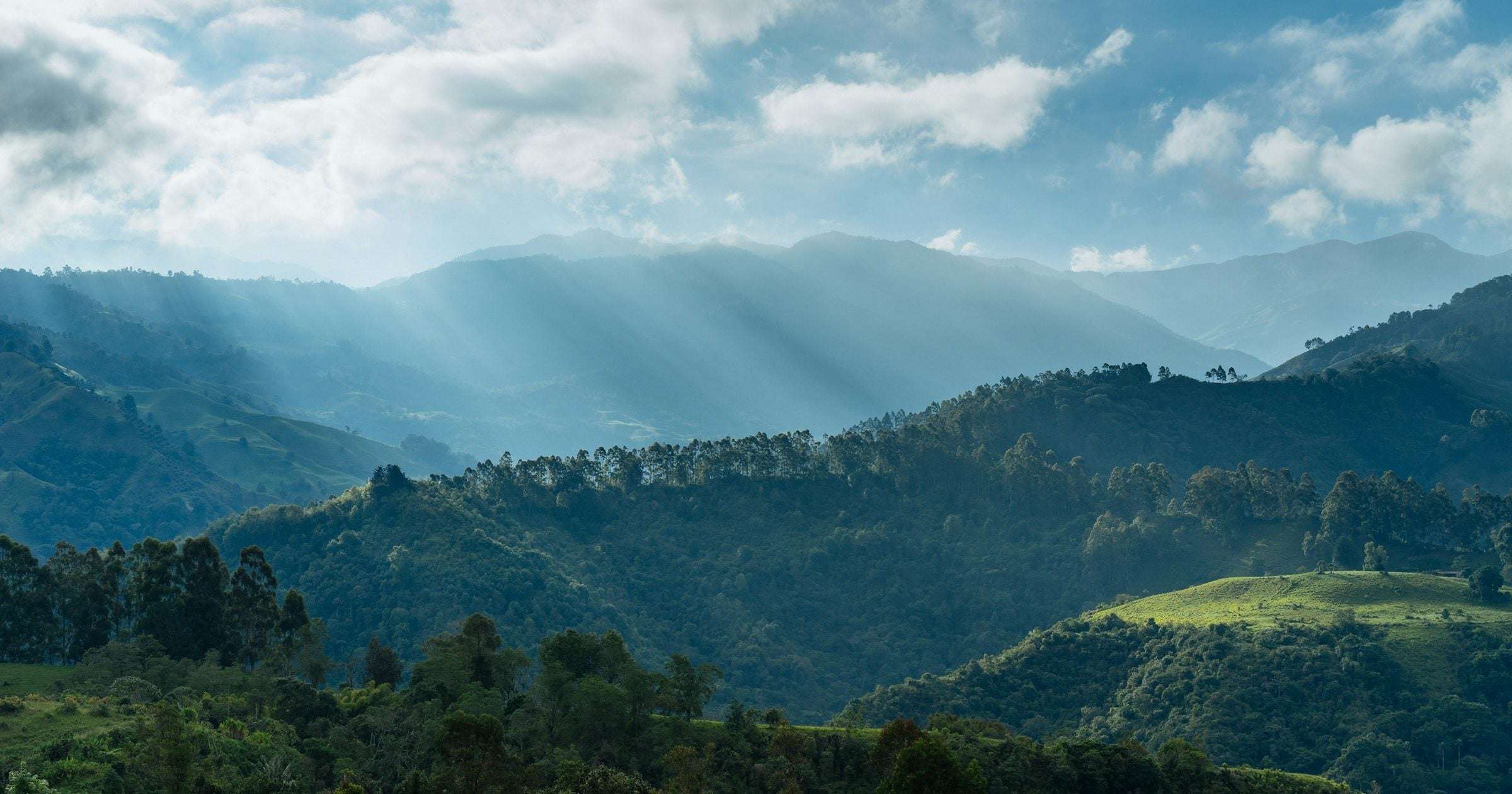 Sunrise rays over Andean ridges and forested hills in Colombia — a popular South American destination where travellers in 2026 plan multi-city trips through Bogotá, Medellín and Cartagena.