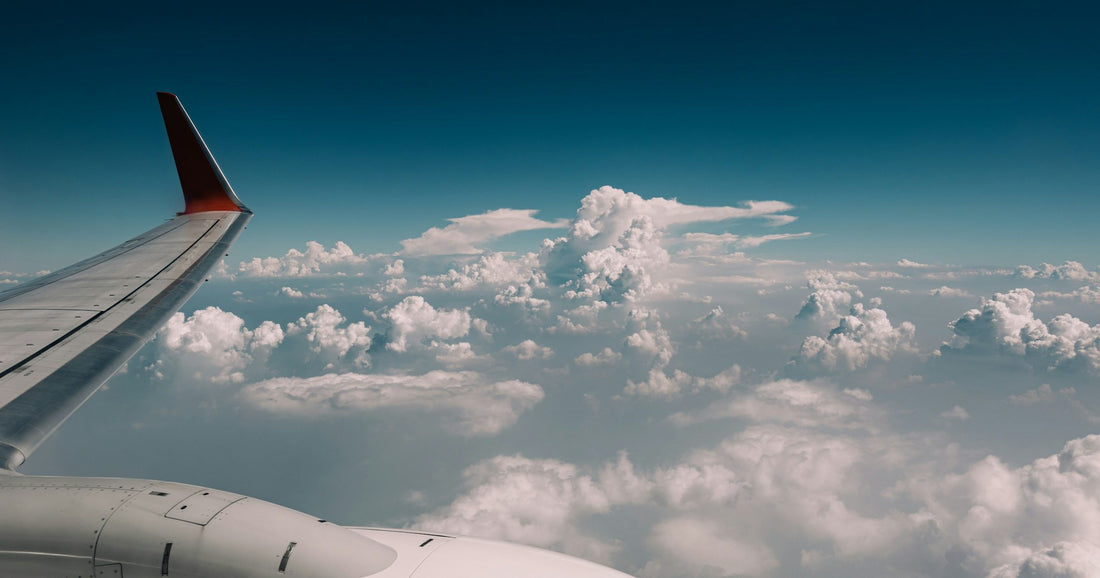 Airplane wing above a sea of dramatic white clouds, evoking international travel between the US and Latin America.