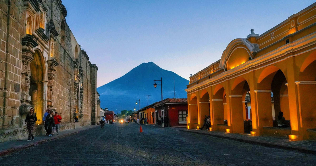 Cobblestone street in Antigua, Guatemala at dusk, framed by colonial yellow architecture and the silhouette of Volcán de Agua — a popular destination on Latin America itineraries.