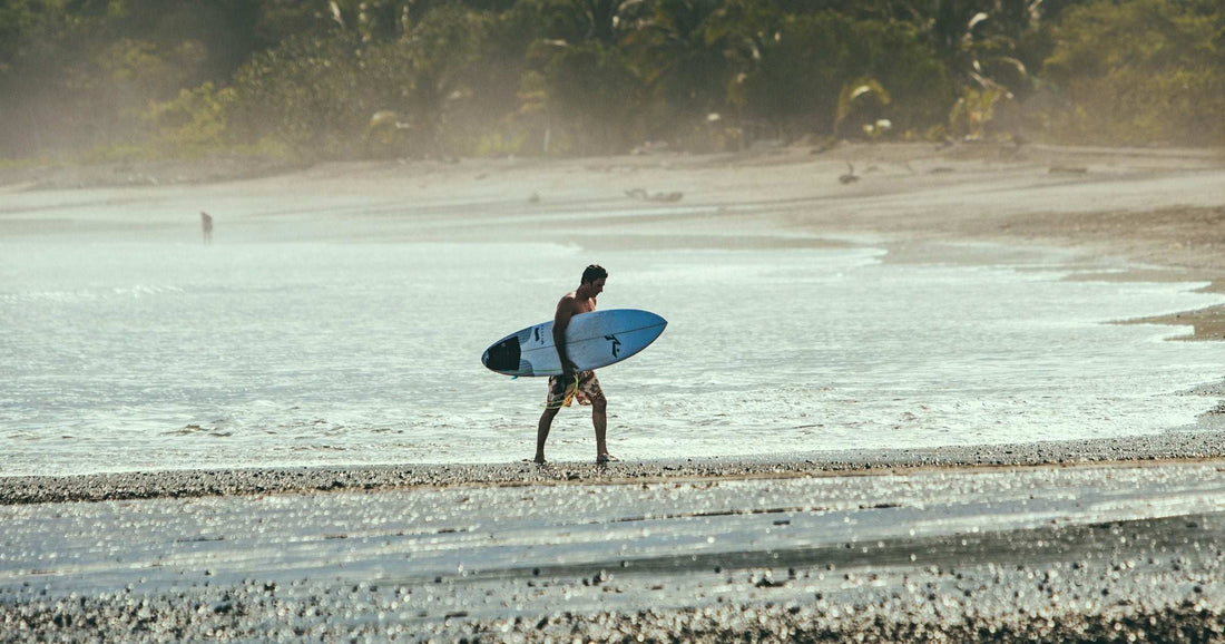 A surfer walks a sandy Central American beach with white surfboard at golden hour — popular surf destination for travellers staying connected with a Panama eSIM.