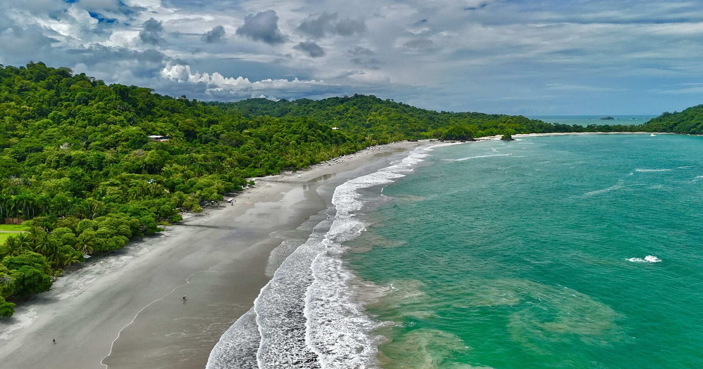 Aerial view of a Costa Rican Pacific coast beach lined with rainforest — Costa Rica ranks #1 in Central America's Global Peace Index in 2026.