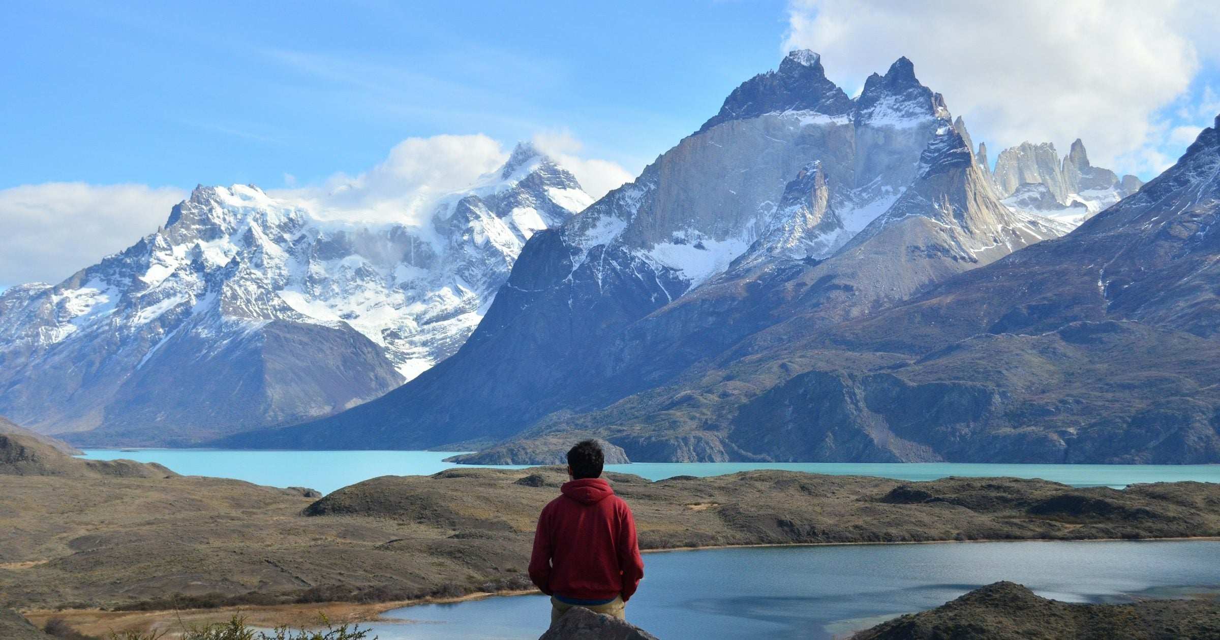 Solo traveller in a red hoodie sitting on a rock contemplating Torres del Paine's Cuernos peaks and turquoise lake in Chilean Patagonia — a popular safe destination for solo travellers in South America.