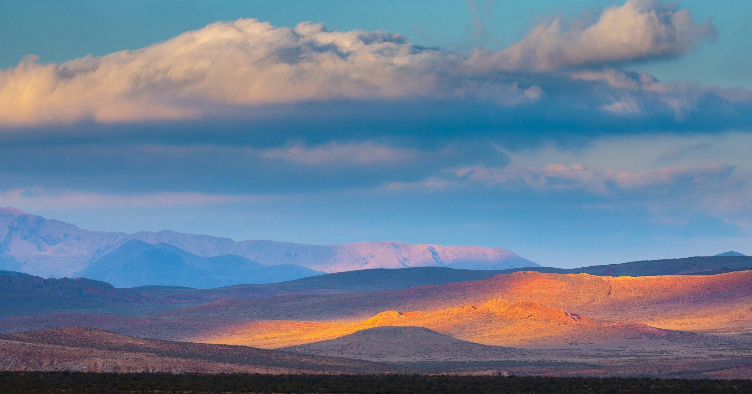 Dramatic sunset light over orange hills and gathering clouds in the South American highlands — weather varies by country across May 2026.
