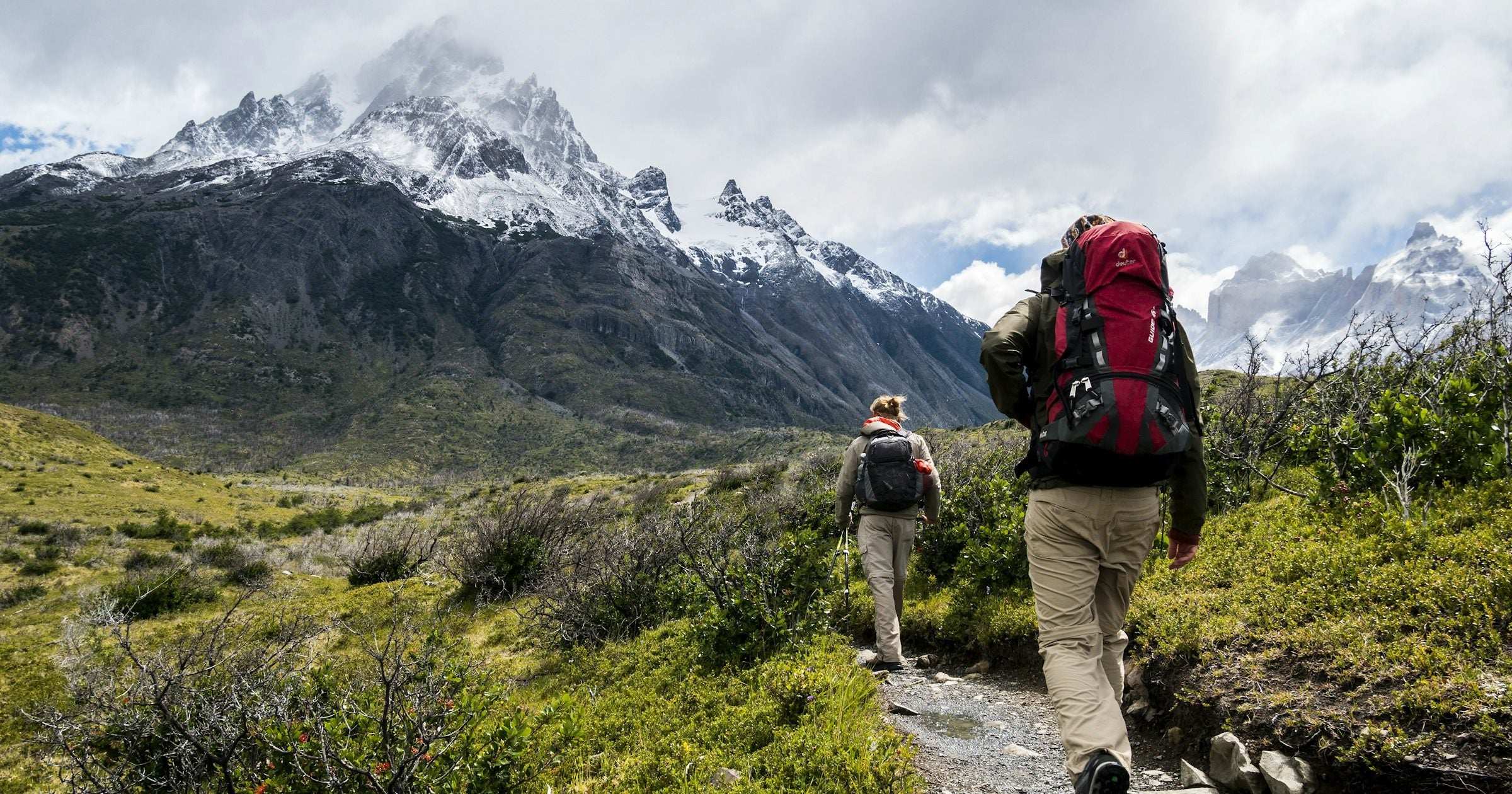 Two backpackers walk together along a Patagonia trail beneath snow-capped peaks in South America — a region with destinations generally considered safe for travellers.