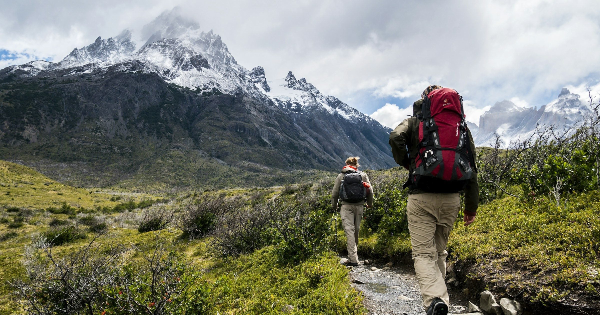 Two backpackers walk together along a Patagonia trail beneath snow-capped peaks in South America — a region with destinations generally considered safe for travellers.